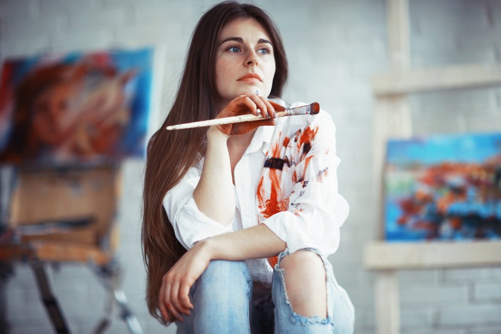 young artist with paint on white shirt with canvases in the background