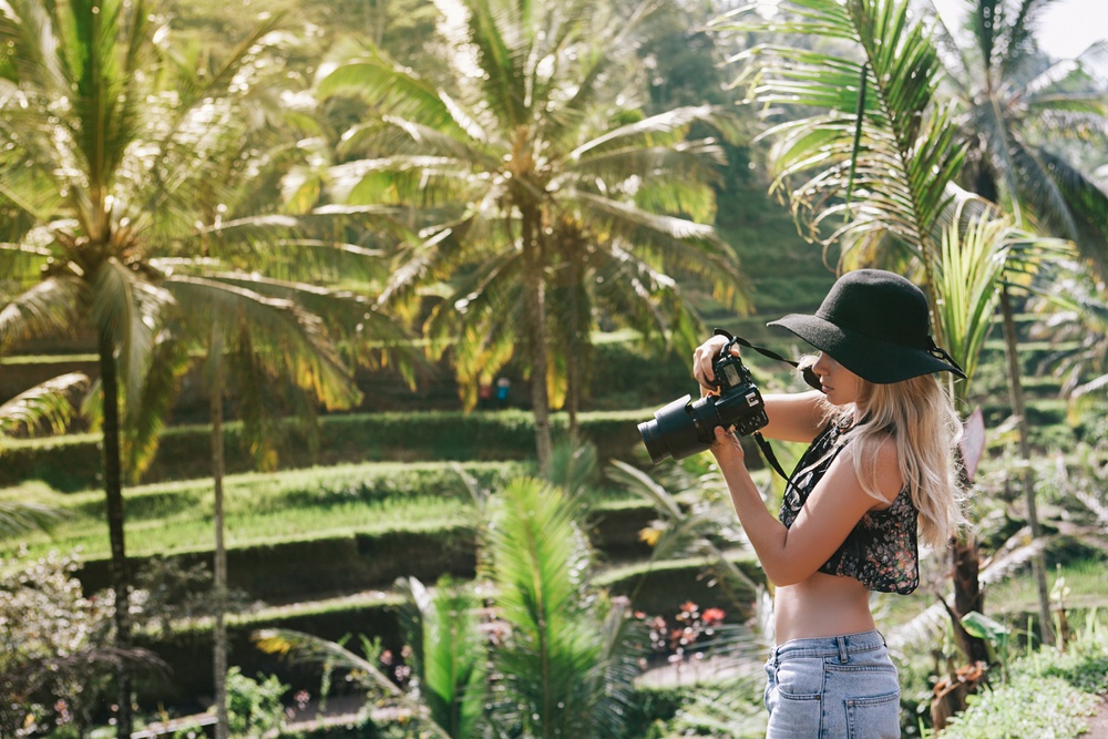 young blonde with short shirt looking at dslr camera in jungle garden setting