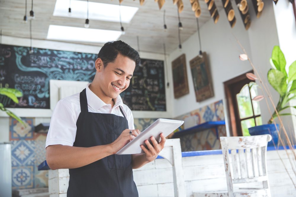 young latino man in cafe managing his business on a tablet