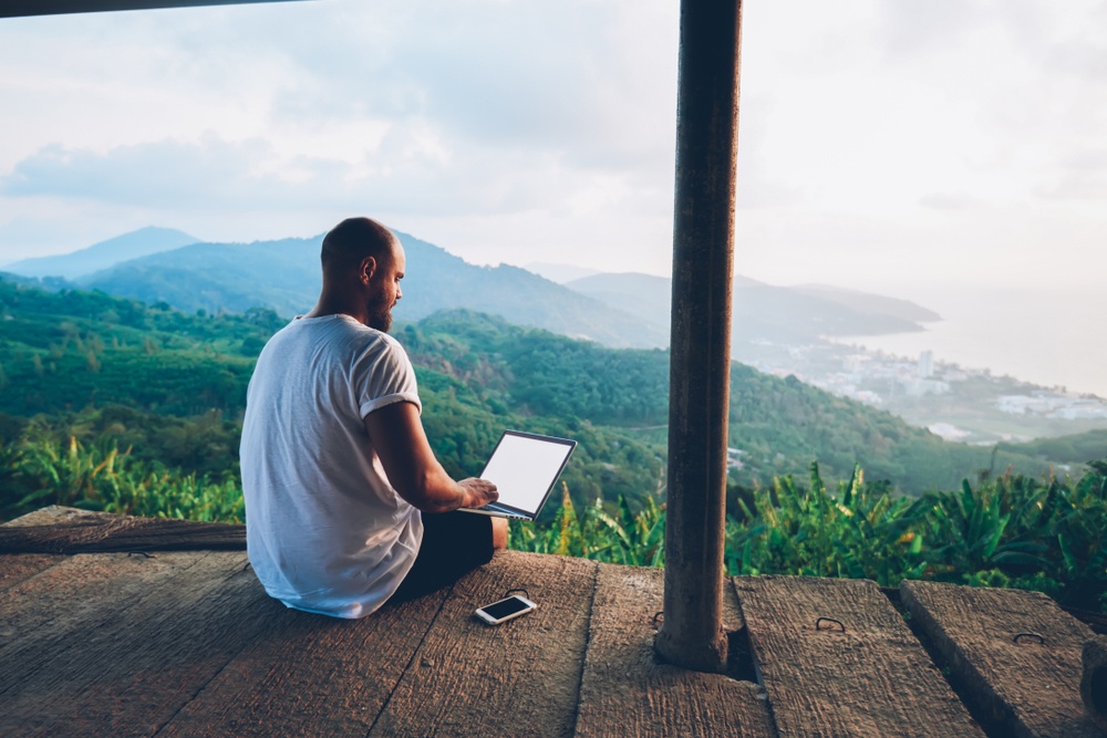 young man wish shaved head and beart sitting on deck above mountains