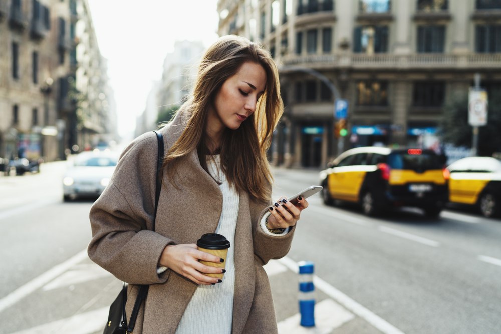 young woman looking seriously at phone in the middle of traffic in the city