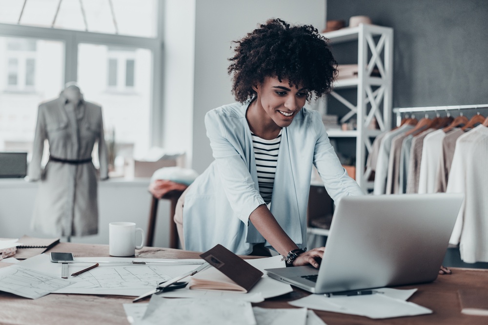 young woman managing retail clothing or fashion business on laptop with notes