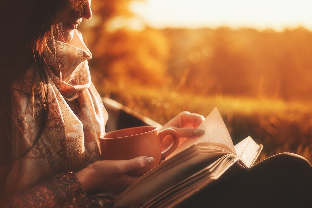 young woman reading a book at sunrise with cup of coffee