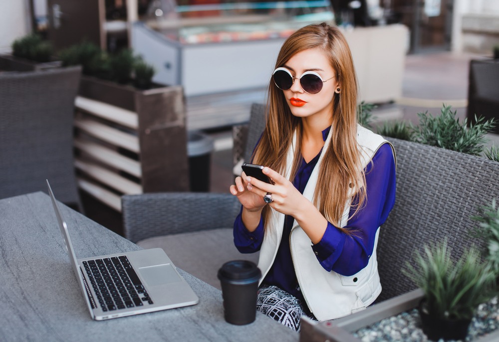 young woman with fashionable sunglasses reading online blog about fashion