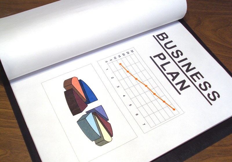 This photo shows an open business plan with a line chart and a pie chart lying on a wooden table, representing the best business plan affiliate programs.