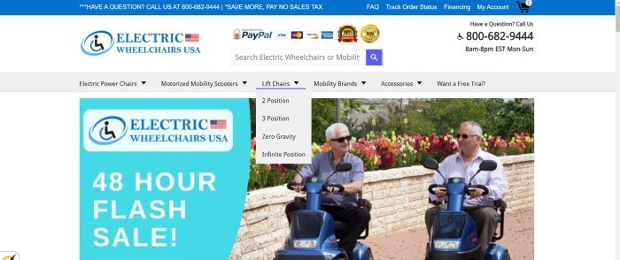 This screenshot of the home page for Electric Wheelchairs USA has a blue announcement bar, a white search bar, a gray navigation bar, an aqua section on the left side of the page announcing a flash sale, and a photo on the right side of the page showing two elderly gentlemen in gray polo shirts and sunglasses riding mobility scooters on a sidewalk next to a flowerbed with yellow, orange, red, and pink flowers.