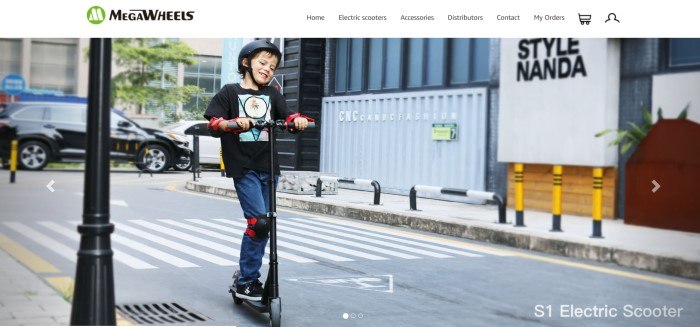 This screenshot of the home page for MegaWheels has a white navigation bar with black text above a photo of a young boy in a black shirt, black helmet, and jeans riding a black electric scooter down a city street.