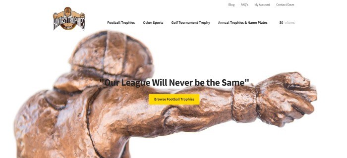 This screenshot of the home page for Fantasy Trophies has a white background and header with a brown and red logo, above a closeup photo of a bronze trophy, along with black text and a yellow call to action button.