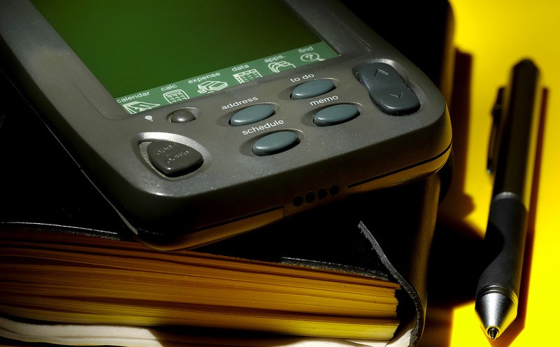 This photo shows a mobile device lying on a black organizer on a yellow table, beside a black pen, representing the best organizer affiliate programs.