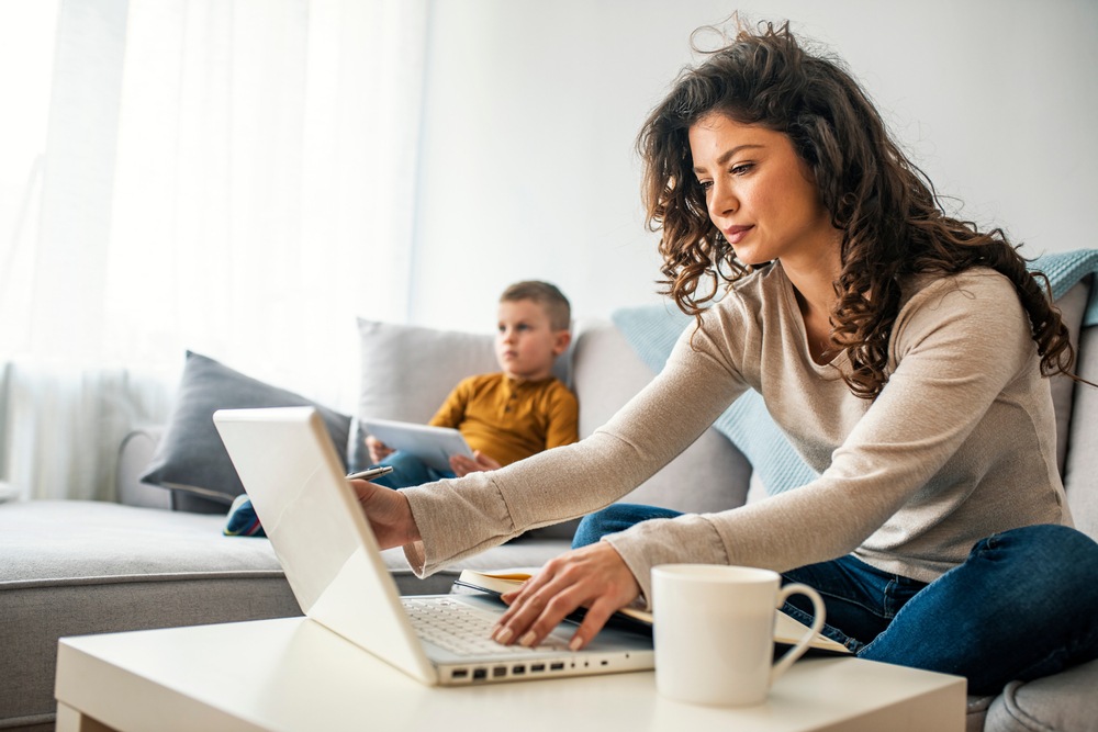 home office with mom doing online work while son sits on sofa