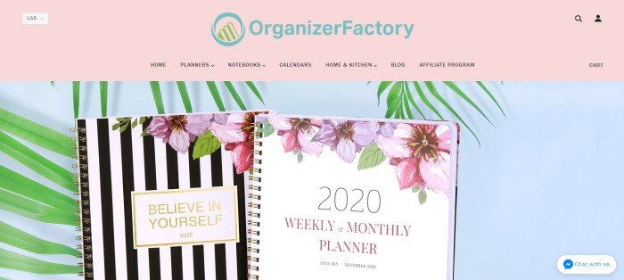 This screenshot of the home page for Organizer Factory has a pink navigation bar above a photo of a black and white striped journal with a floral design and a 2020 planner with a white background and floral design against a white background with green leaves.