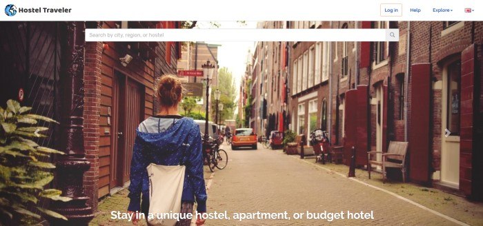 This screenshot of the home page for Hostel Traveler has a white header and search bar overlaying a photo showing the back of a woman in a blue jacket walking down a narrow European street.