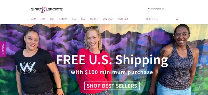 This screenshot of the home page for Skirt Sports has three women in feminine workout clothing, including tee shirts and running skirts, standing in front of a painted backdrop of purple mountains, and white text that announces free U.S. shipping with a 0 minimum purchase.