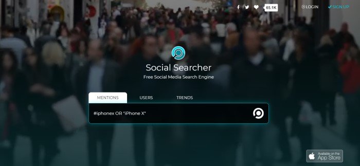 This screenshot of the home page for Social Searcher has a dark filtered, blurred screenshot of a people-crowded street, behind an aqua logo, white text, and a black search bar.