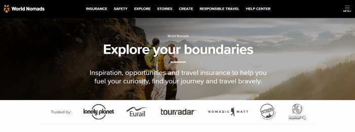 This screenshot of the home page for World Nomads has a black navigation bar with white text above a large photo showing two young travelers in coats and backpacks looking out over a misty valley, behind white text and above a white section with black logos of partner companies.