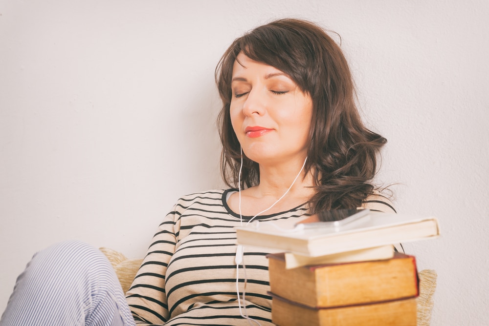 woman listening to audiobook with stack of physical books by her side