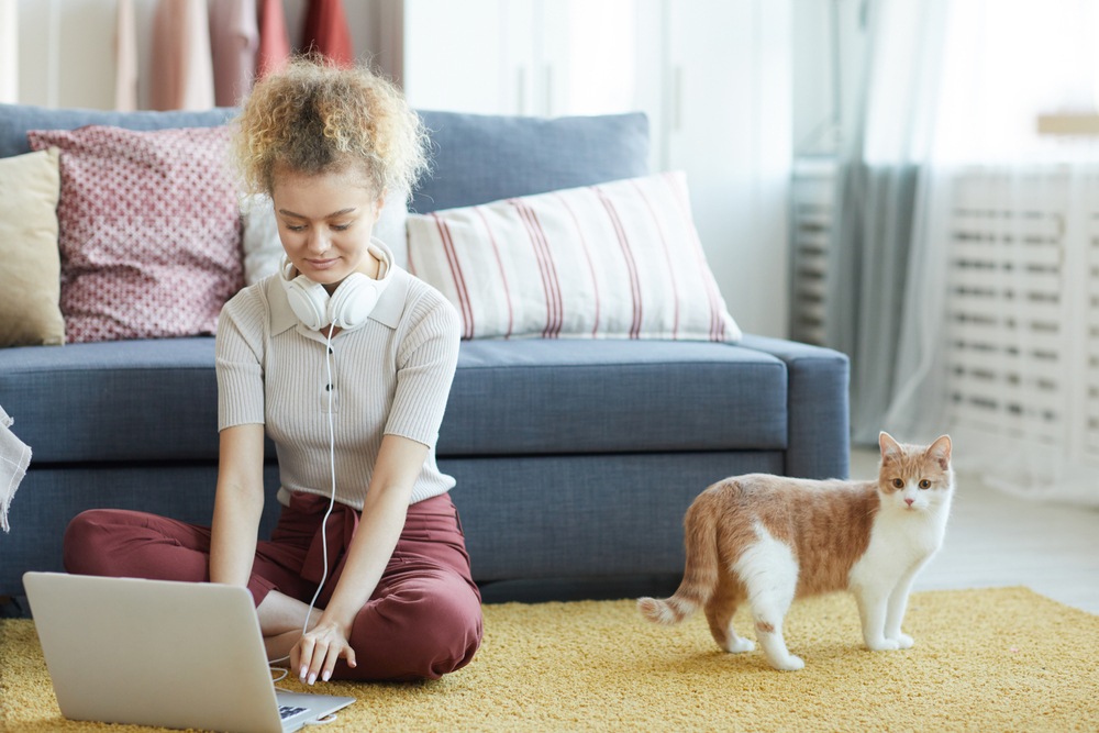 young woman sitting on the floor doing online transcription work with her cat