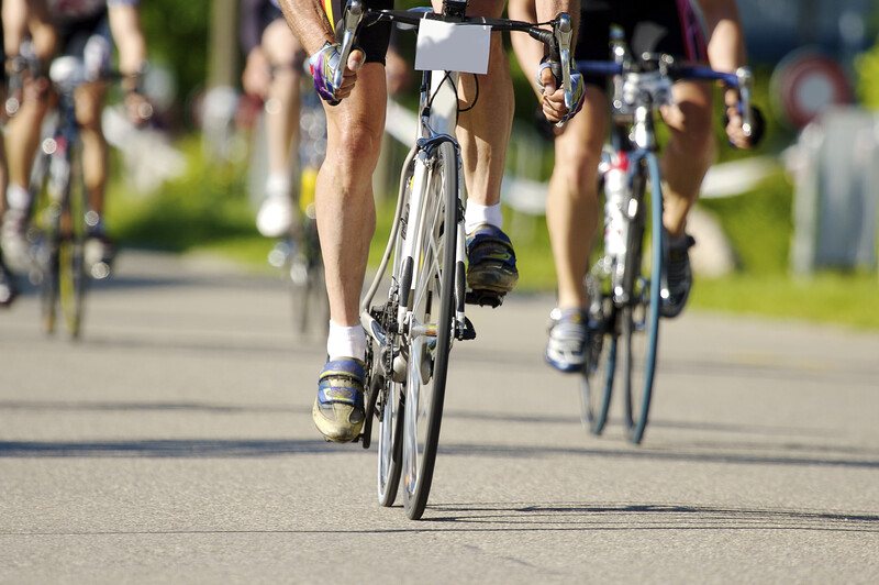 This photo shows the legs of four people riding street bikes in a race on pavement near a green grassy area, representing the best bicycle affiliate programs.