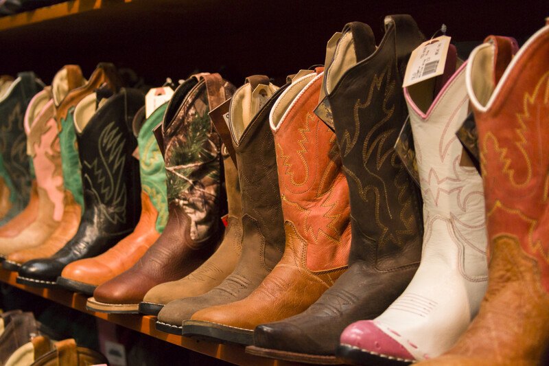 This photo shows a row of cowboy boots in varying shades of brown white, and black on a shelf in a shoe store, representing the best boots affiliate programs.