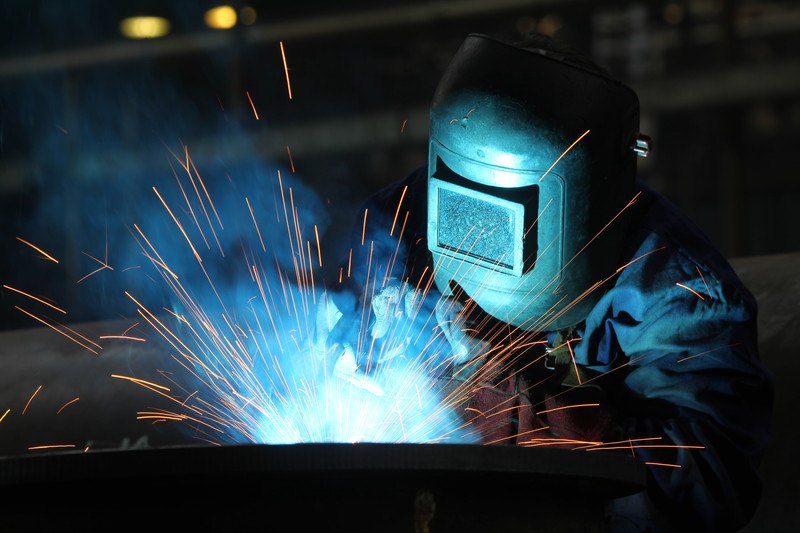 This photo shows a man in a welding helmet welding something while orange sparks fly out in several different directions, representing the best welding affiliate programs.