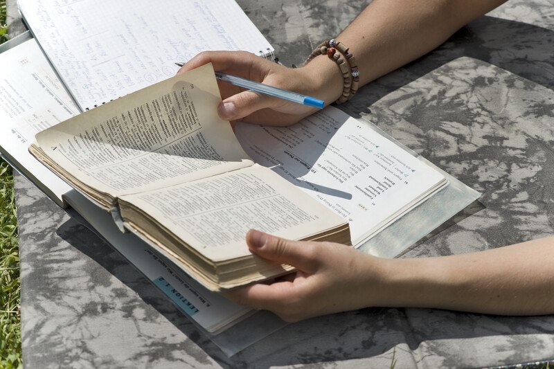 This photo shows a woman's hands holding a pen and an open dictionary over a binder, as if she is studying different words to use when translating text from one language to another.