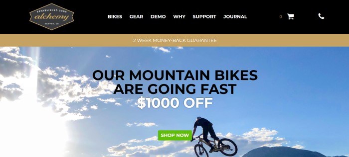 This screenshot of the home page for Alchemy Bicycles has a black and gold header and navigation bar with white and gold text above a photo showing a cyclist on a mountain bike against a blue sky with white clouds, behind black and white text with a green call to action button.