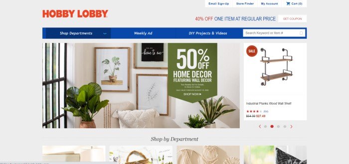 This screenshot of the home page for Hobby Lobby has a gray background, a red logo in the upper left corner, a blue navigation and search bar with white text, a photo showing green plants and photos of green plants on a wall, along with a green text section with white text announcing a sale, and a photo on the right side of the page of a set of hanging shelves.