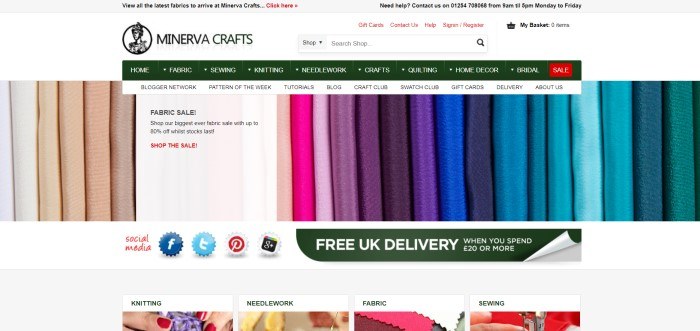 This screenshot of the home page for Minerva Crafts has a gray header, a white search bar, a dark green navigation bar, and a photo showing rows of fabric in varying solid colors ranging from white to teal, above a bar showing social media icons and a dark green announcement for free delivery, and a row of small photos with text depicting categories of items this store carries.