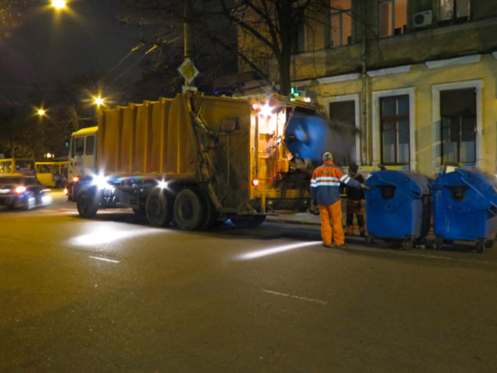 trash collectors picking up dumpsters at night