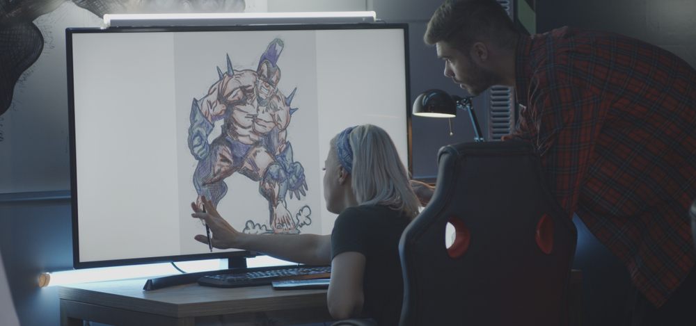 two video game designers looking at sketch of video game character on big computer screen