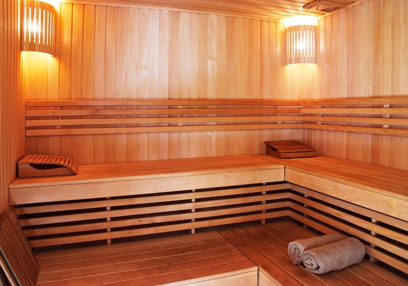 This photo shows the inside of a wooden cabinet-style sauna with two lit lamps in the corners, representing the best sauna affiliate programs.