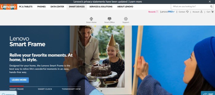 This screenshot of the home page for Lenovo has a black header, a white navigation bar with black text and an orange logo, above a gray secondary navigation bar, and a large photo of a woman in a blue hat putting a frame around a picture of a young girl and a woman cutting a birthday cake, along with white text and a blue call to action button.