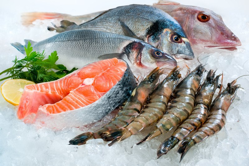 This photo shows a variety of fish, a salmon fillet, some fresh shrimp, and a lemon wedge with dill and parsley on a bed of ice, representing the best seafood affiliate programs.