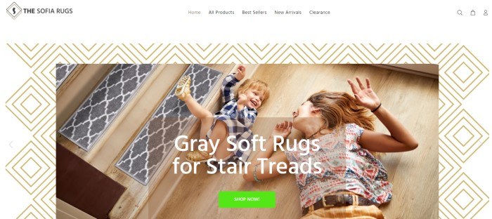 This screenshot of the home page for The Sofia Rugs has a white navigation bar with black text above a main section that includes a background with gold-outlined nested white squares and a photo of a smiling mom and toddler lying on a wooden floor next to wooden stairs with gray and white stair treads on them, as well as white text and a green call to action button.