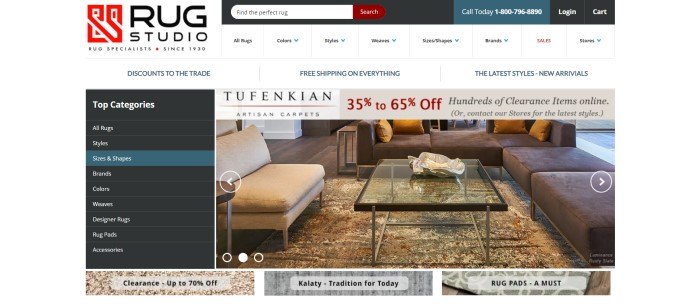 This screenshot of the home page of Rug Studio has a dark search bar above a white navigation bar, with a black category column on the left side of the main section of the page and a photo of a living room with a glass coffee table on a large beige, cream, and red area rug.