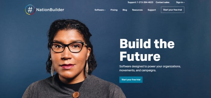 This screenshot of the home page for NationBuilder has a dark blue background with white text in the navigation bar and on the right side of the page, along with a photo of a dark-haired woman in glasses and a gray sweater on the left side of the page, and a blue call to action button.