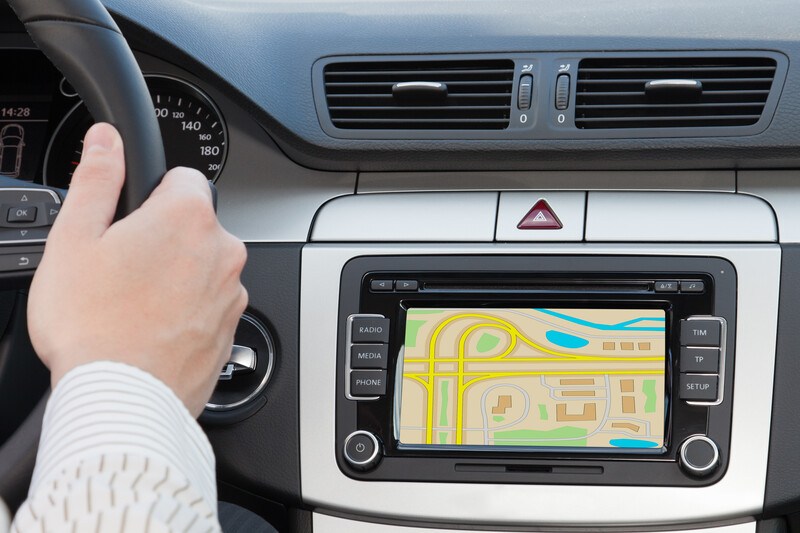 This photo shows a multicolored screen on a GPS unit installed in a luxury vehicle, while a man's hand rests on the steering wheel, representing the best GPS affiliate programs.