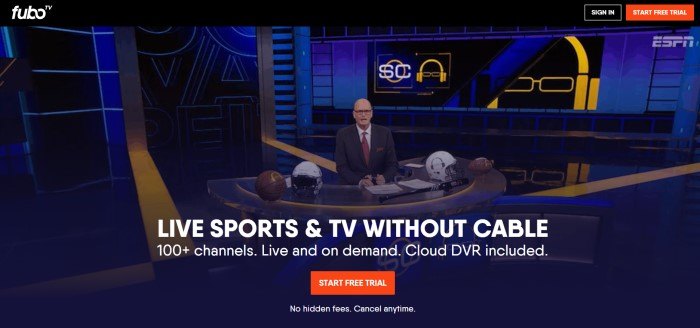 This screenshot of the home page for FuboTV has a large photo of a production studio with blue, black, and yellow elements, as well as a man wearing a suit and glasses behind a desk with four football helmets on it, behind white text and a red call to action button.