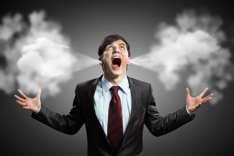 This photo shows a young businessman in a dark suit and red tie, holding his hands out to his sides, looking up, and screaming, while steam comes out of his ears, representing the best anger management affiliate programs.