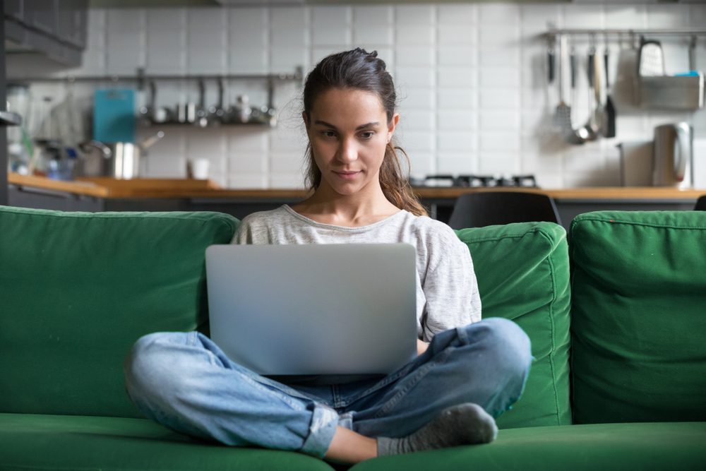 freelancer working from home on a green couch with white tile kitchen in background