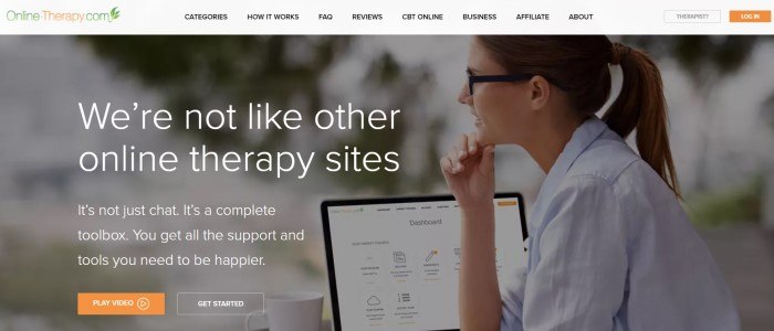 This screenshot of the home page for Online Therapy has a gray header with an orange and green logo above a photo of a smiling woman in glasses sitting in front of an open laptop, behind white text and an orange call to action button.