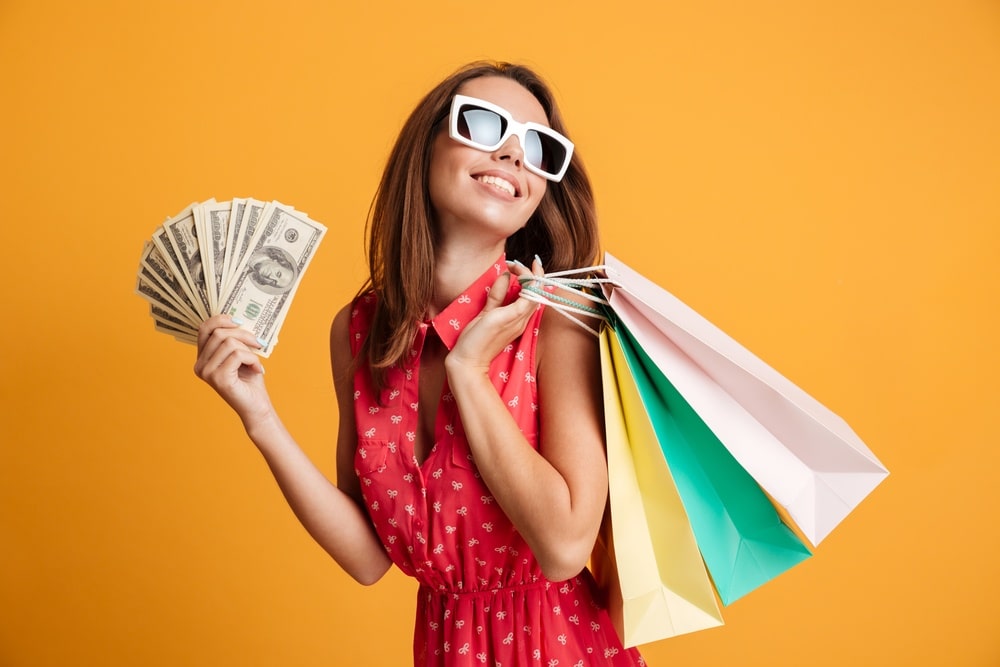 young woman spending money shopping with colorful bags and cash in hand