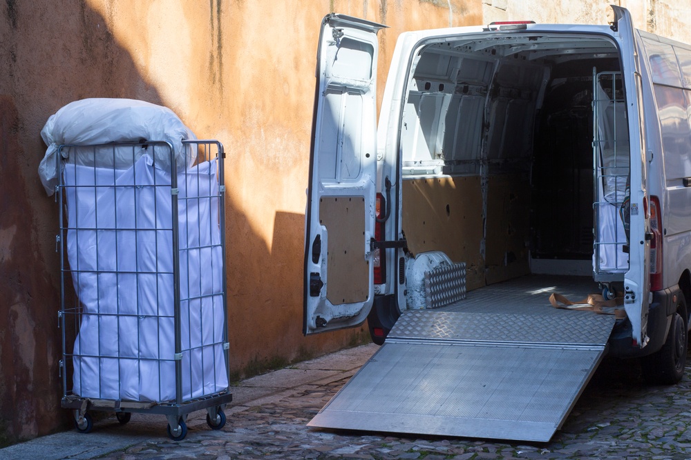 white van with open doors and metal ramp picking up industrial laundry bin