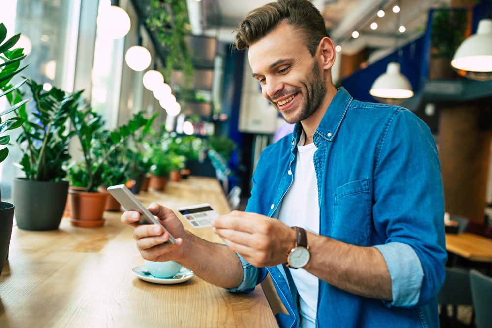 A smiling man holds his credit card and smartphone. 