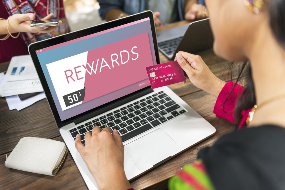 A woman looks at her credit card next to her laptop that is open to a rewards site. 