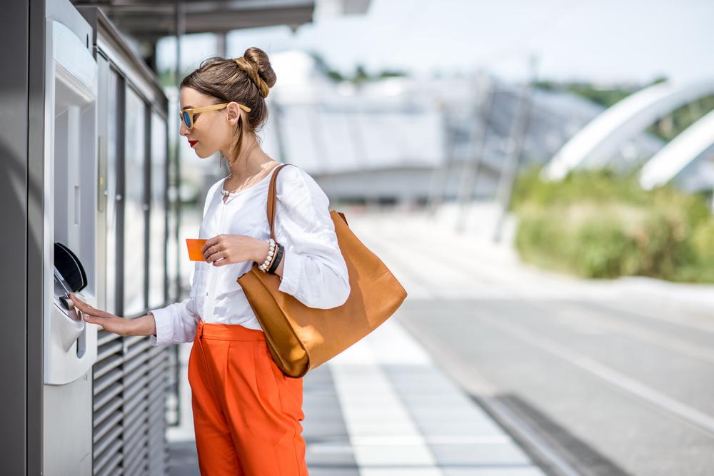 A woman holding a purse uses an outdoor ATM. 