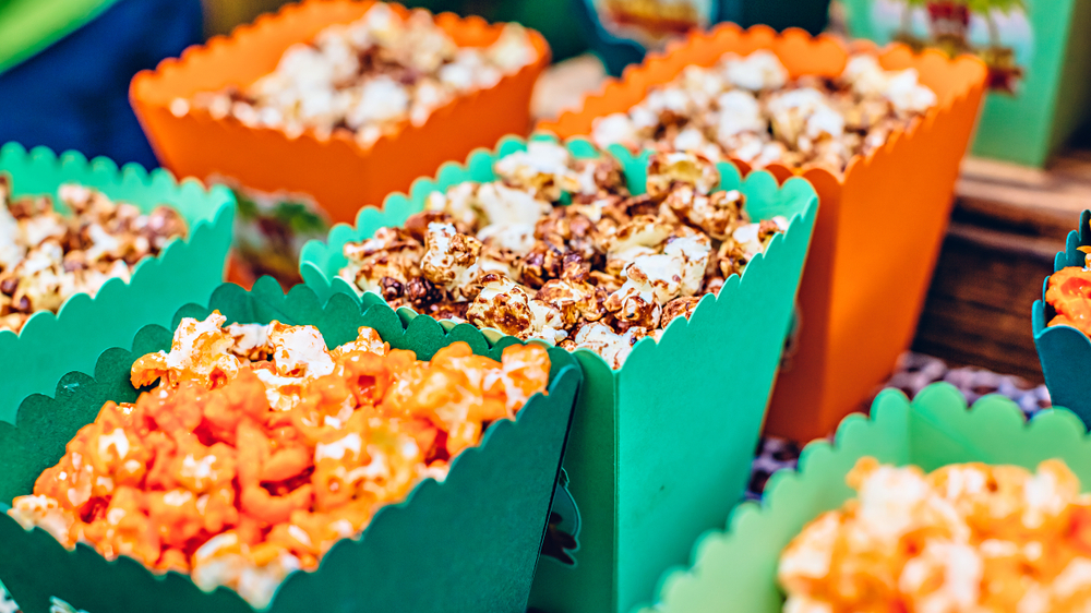 Buckets of different flavors of gourmet popcorn sit side by side in orange and green boxes.
