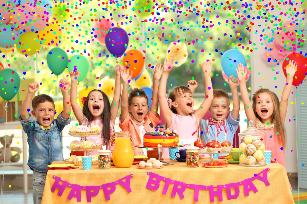 Children raise their hands in happiness at a table that says "Happy Birthday."