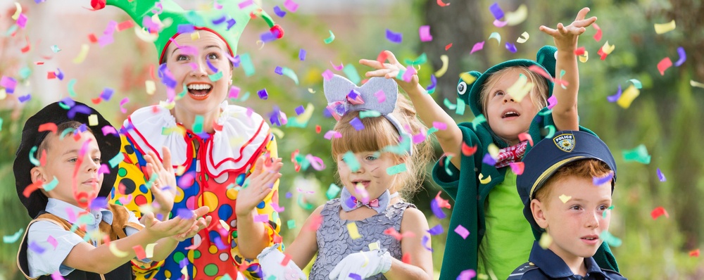 A party clown throws confetti in the air in front of costumed children. 