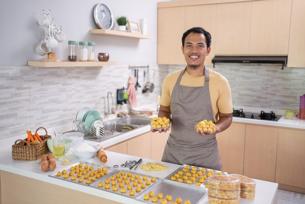 A man with handfuls of baked goods wears an apron in a kitchen. 